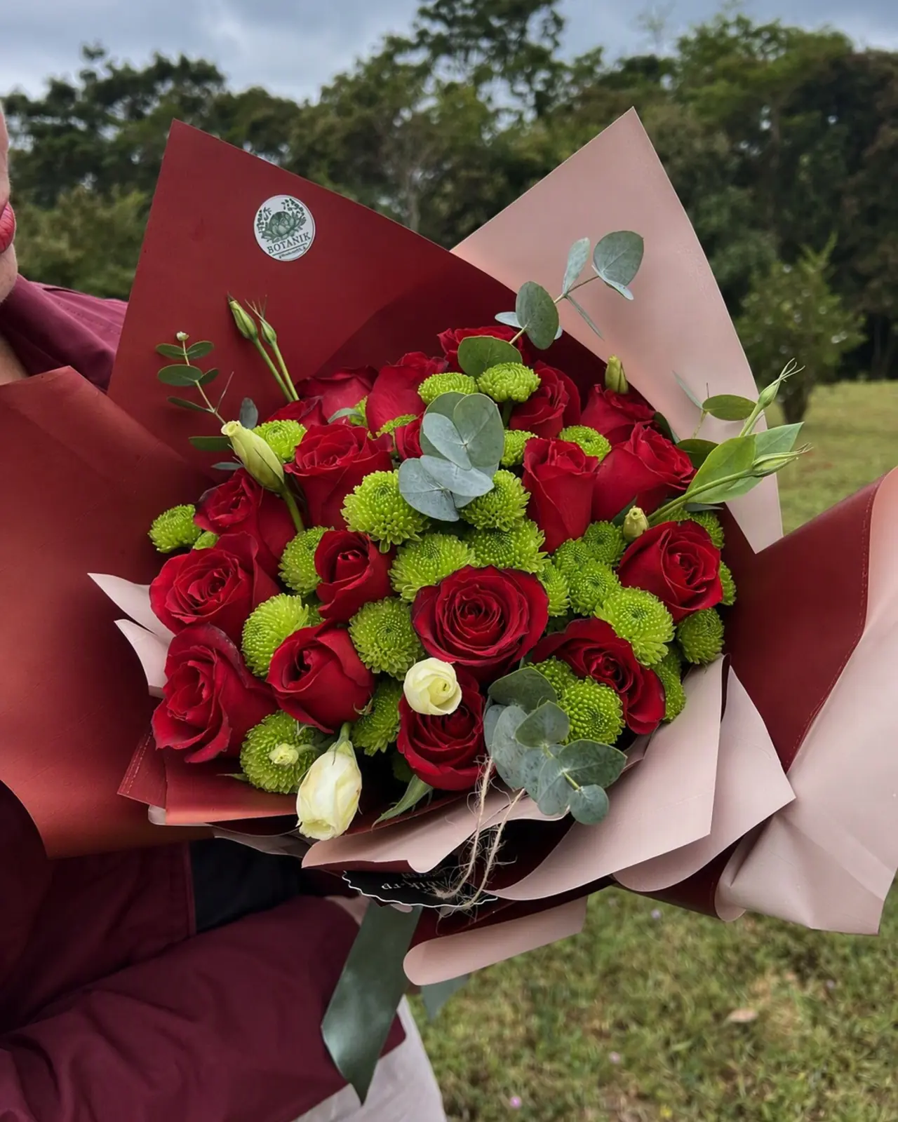 Buquê de rosas magenta, dálias e crisântemos em papel rosa, com o selo da Botanik.
